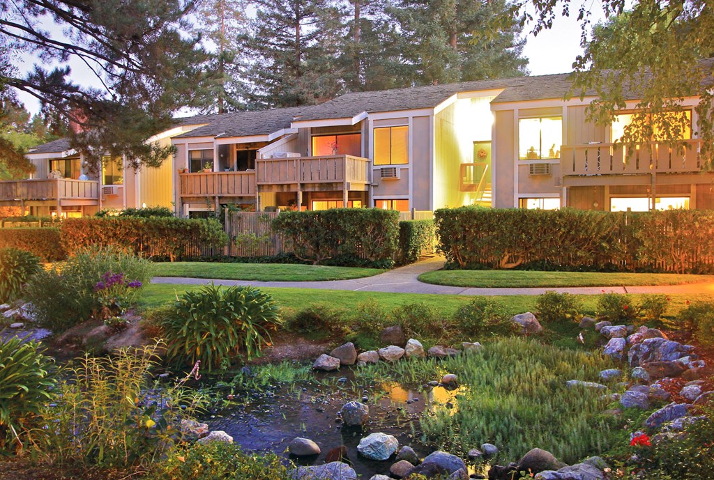 a view of the apartments from a garden with a creek