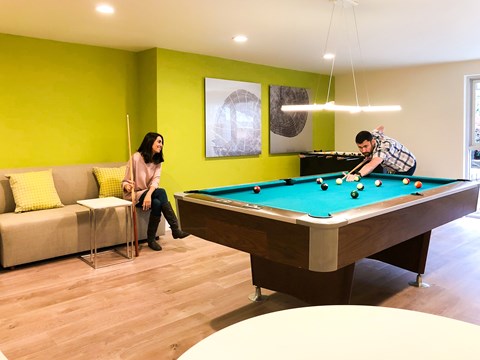 A man and a woman are playing pool in a room with a green wall.