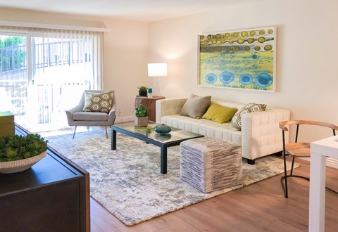 A living room with a white couch, a grey chair, a glass coffee table, and a painting on the wall.