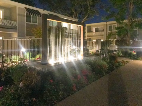 A nighttime view of a well-lit garden pathway leading to a building.