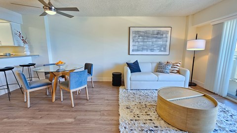 A living room with a white couch, a wooden coffee table, and a dining table with chairs.