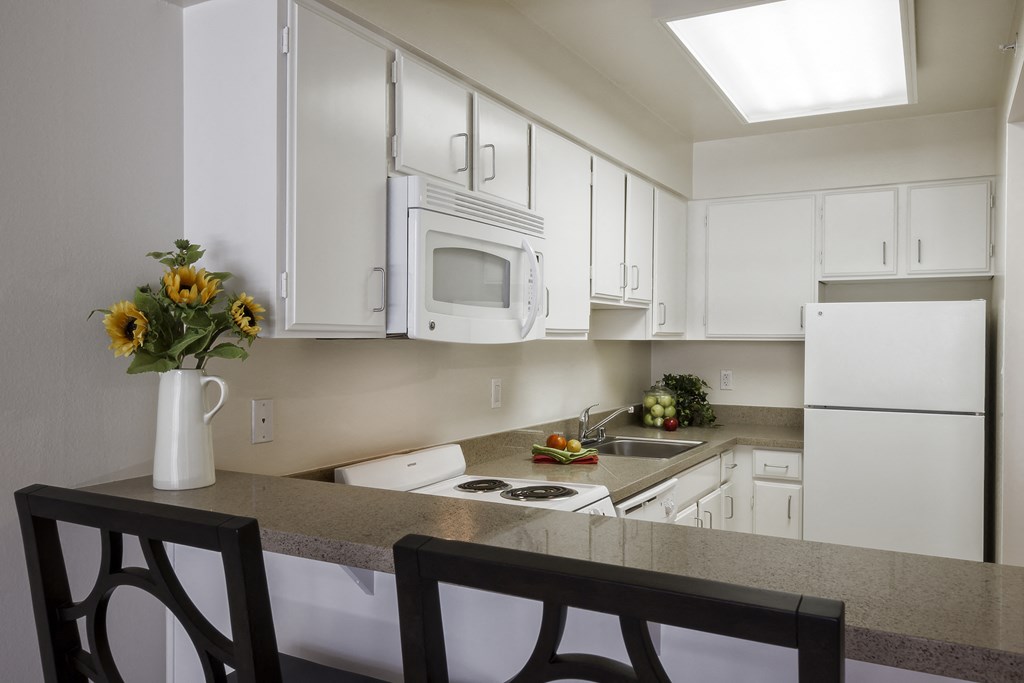 a kitchen with white cabinets and a counter with a vase of flowers
