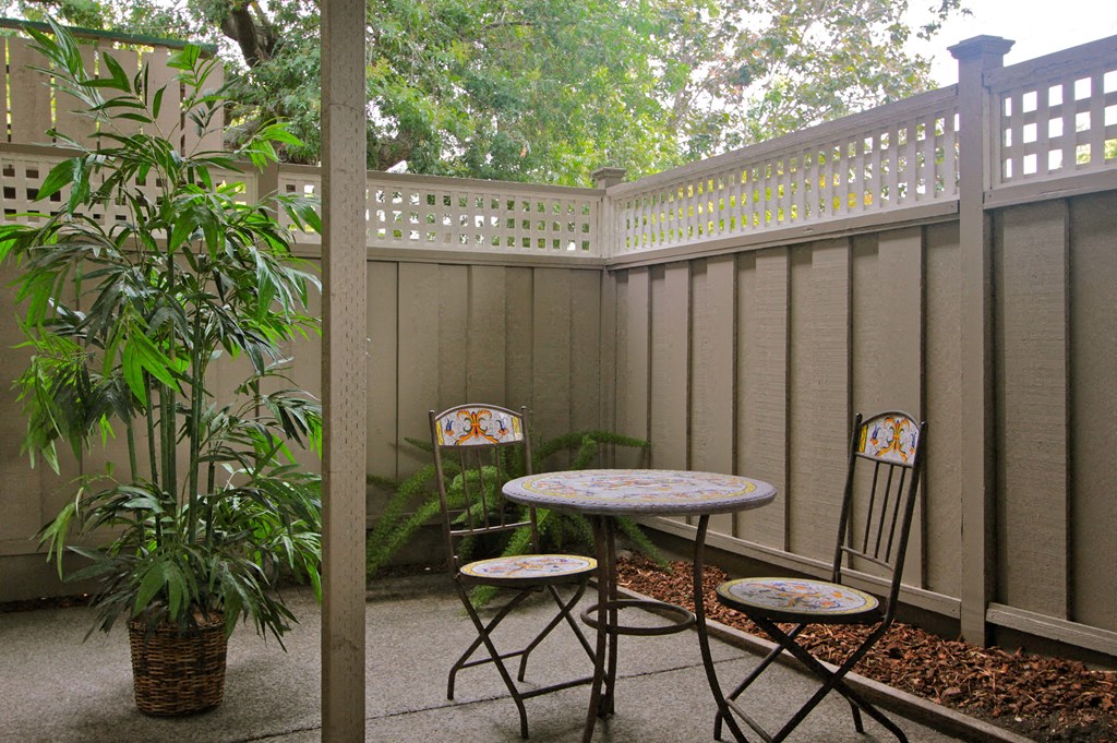 a patio with two chairs and a table in front of a fence