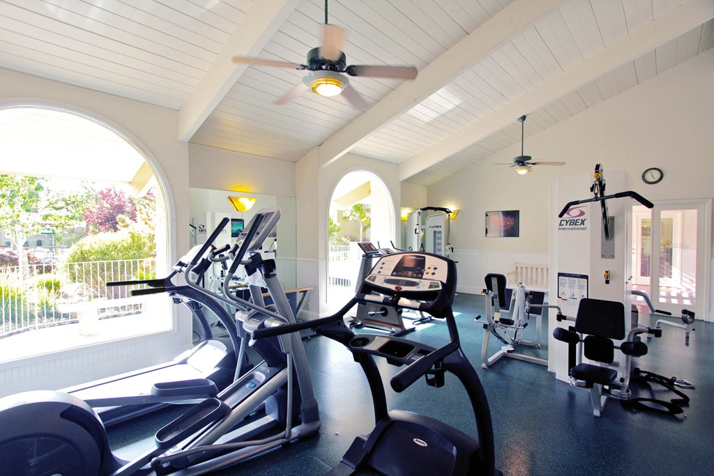a gym with cardio machines and a ceiling fan