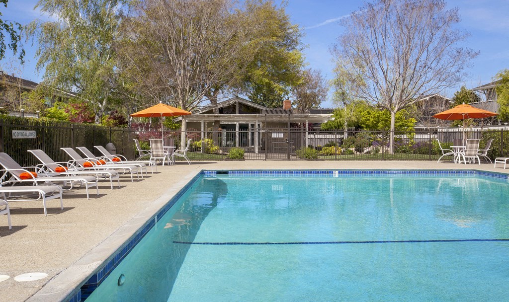 a swimming pool with chairs and umbrellas and a house in the background