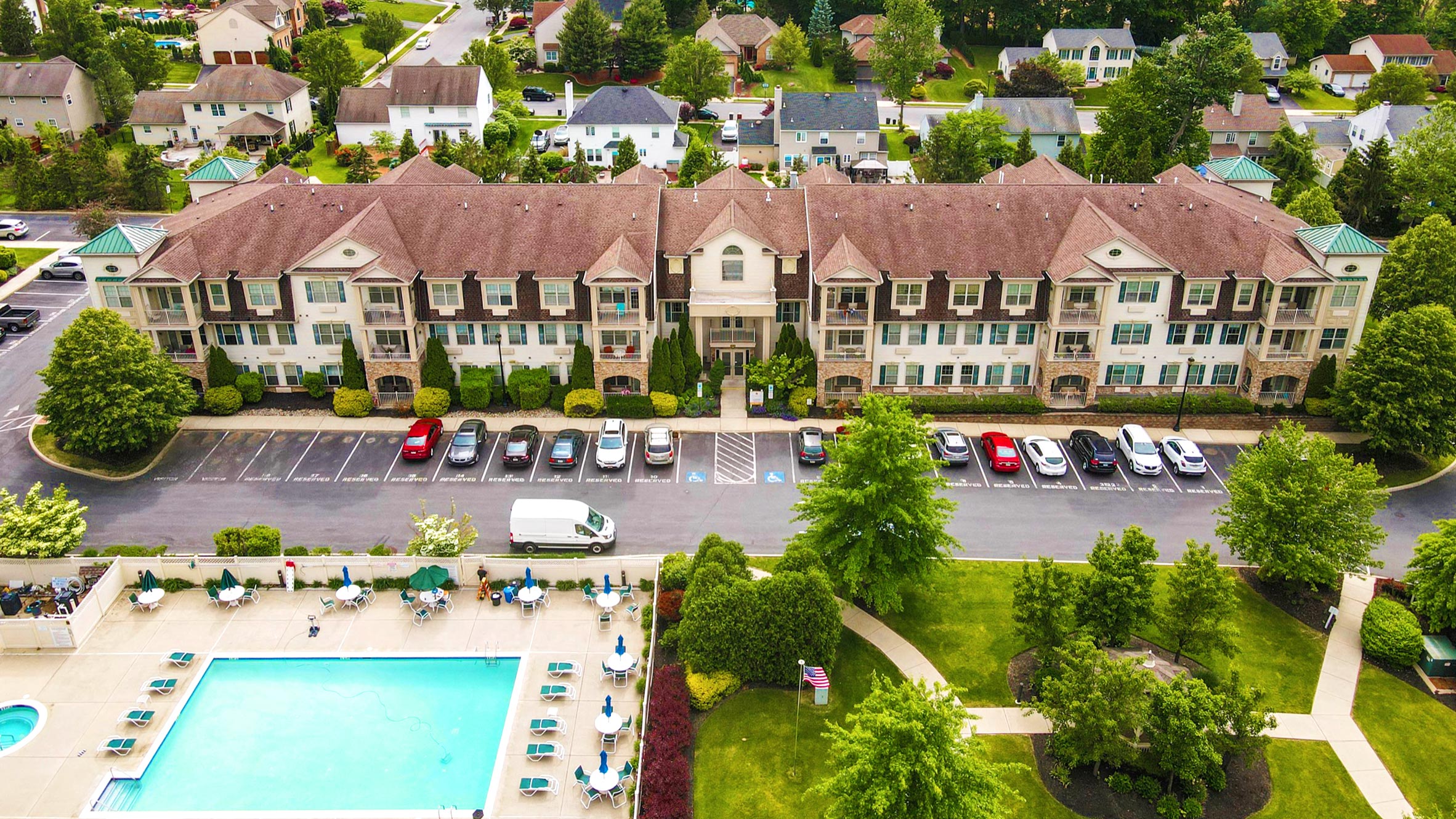 an aerial view of a swimming pool and a parking lot in front of a building