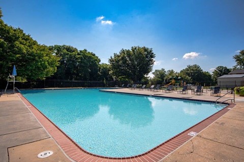 a swimming pool with chairs and trees in the background
