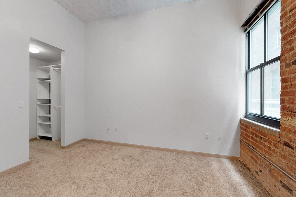 an empty room with a brick wall and a window and a closet