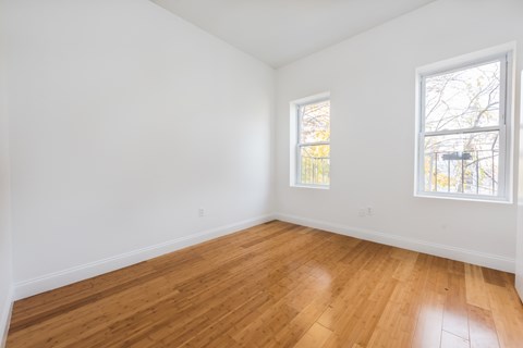 an empty room with wood floors and two windows