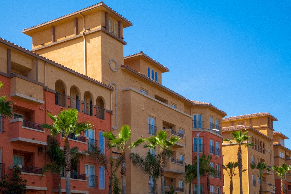 A building with a red and beige facade with balconies and palm trees in front.