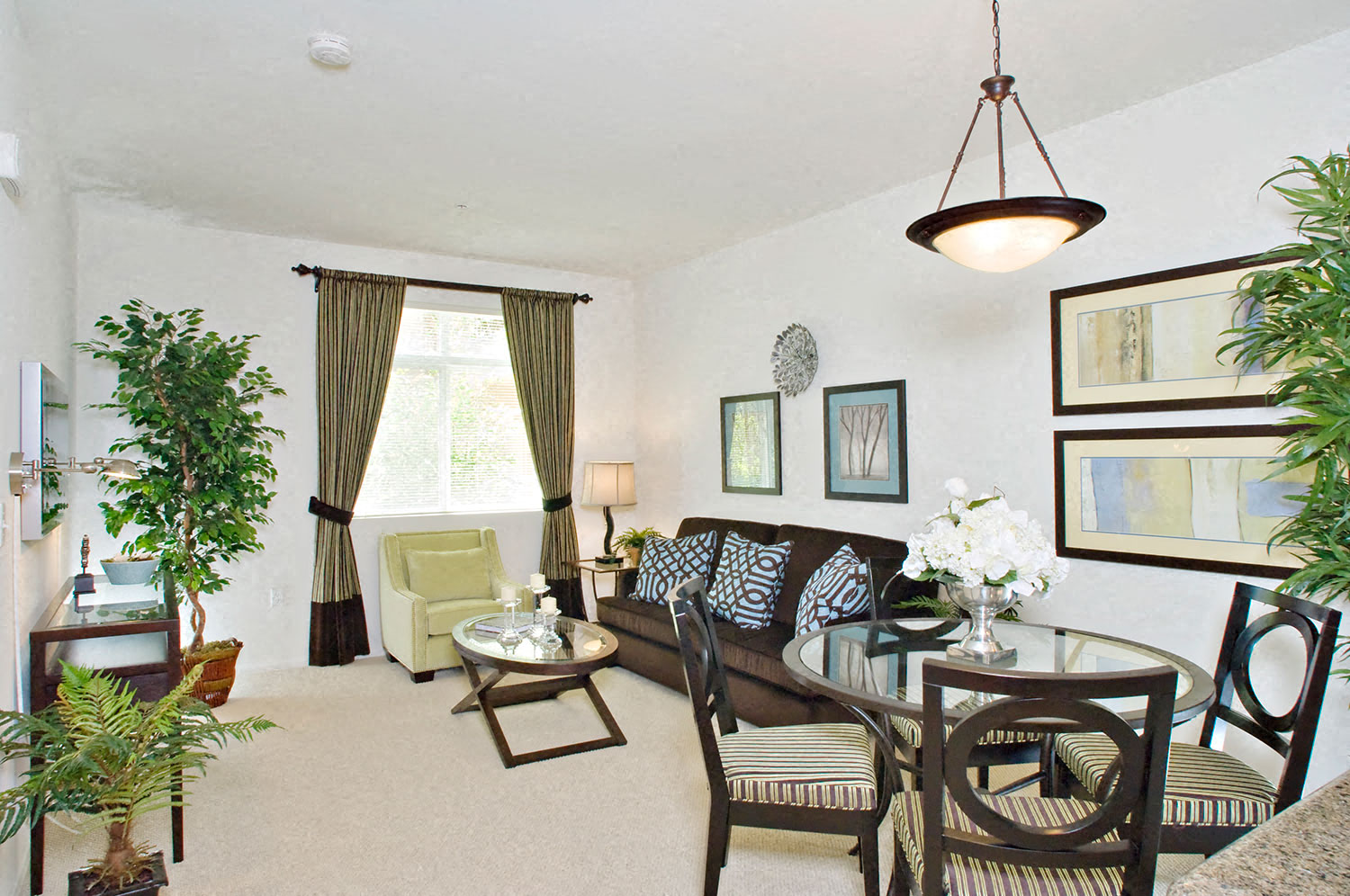 A living room with a brown couch and a glass table.