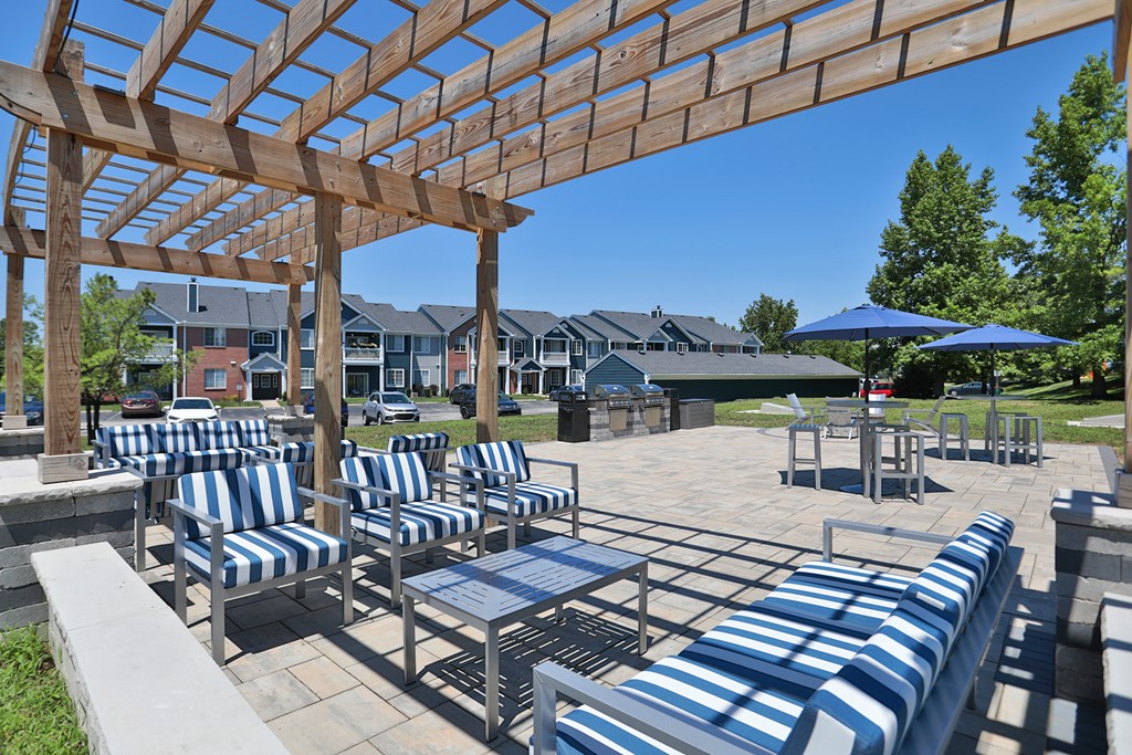 A wooden pergola over a patio with blue and white striped chairs.