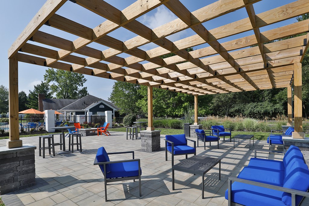 a patio with blue chairs and tables under a wooden pavilion