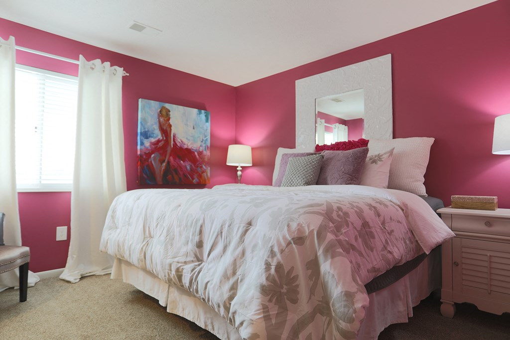 a bedroom with pink walls and a bed with a white comforter
