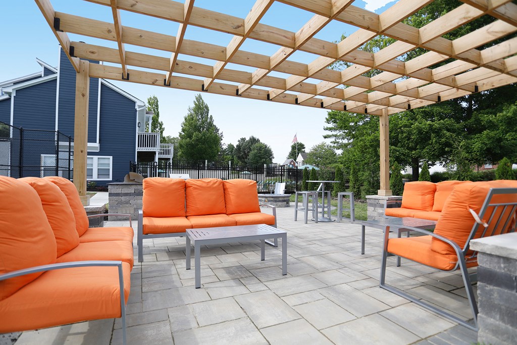 a patio with orange couches and tables under a wooden roof