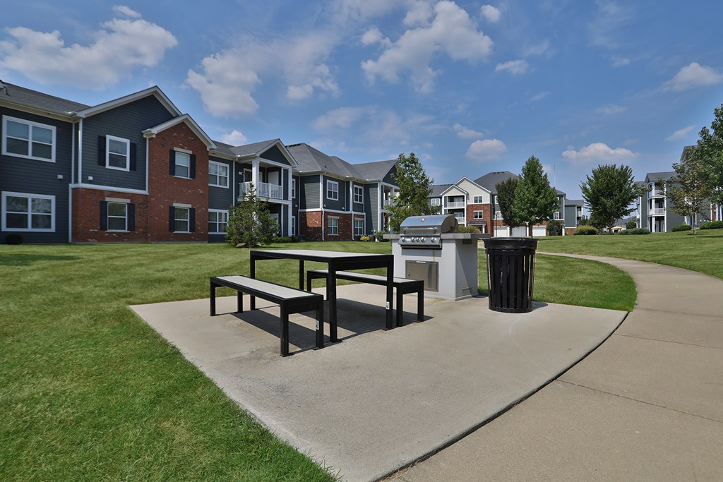 A park area with benches and a trash can in front of apartment buildings.