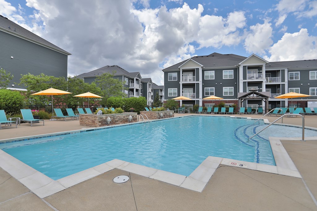 A large swimming pool with a stone wall and a building in the background.