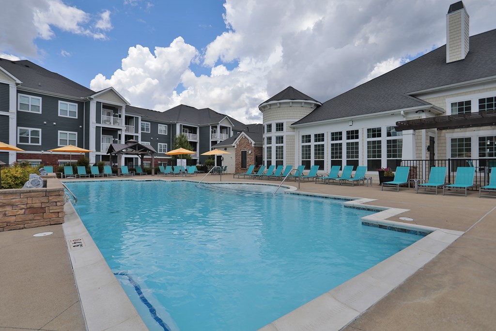 A large swimming pool in front of a building with a stone wall on the left.