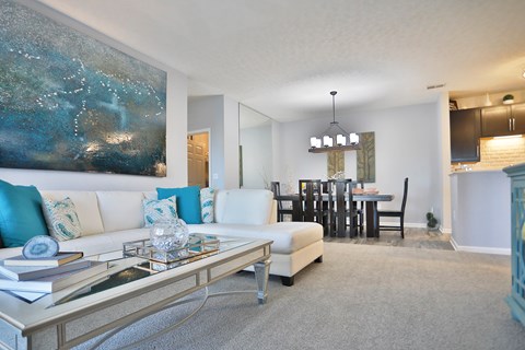 A modern living room with a large painting on the wall and a dining area in the background.