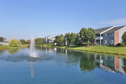 A fountain in the middle of a lake in front of apartment buildings.