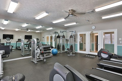 a gym with cardio machines and weights and a ceiling fan