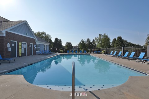 A large outdoor swimming pool with a building to the left and sun loungers on the right.