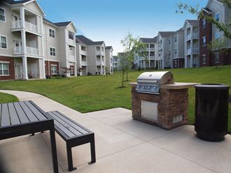 an outdoor kitchen with a grill and a picnic table in front of an apartment complex