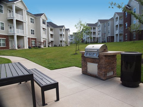 an outdoor kitchen with a grill and a picnic table in front of an apartment complex