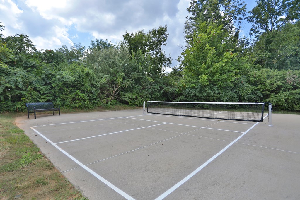 A tennis court surrounded by trees and a bench.