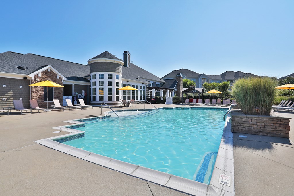 A large swimming pool in front of a building with a yellow umbrella.