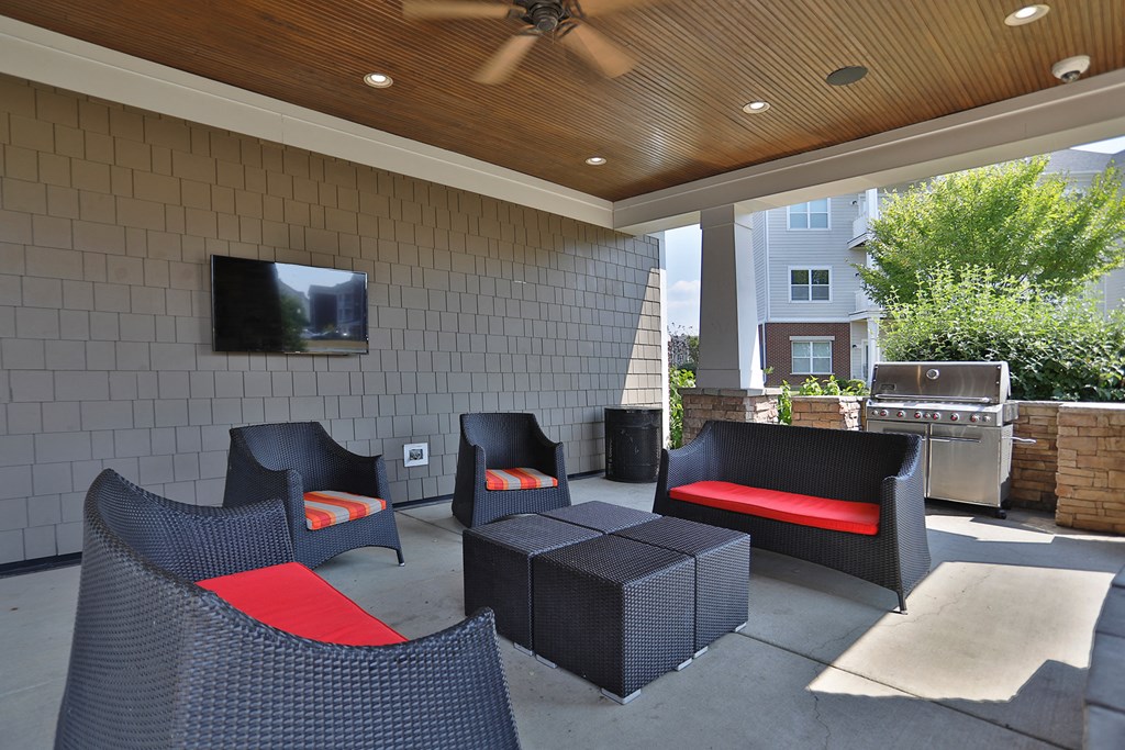 A patio with a black wicker chair and a red cushion.