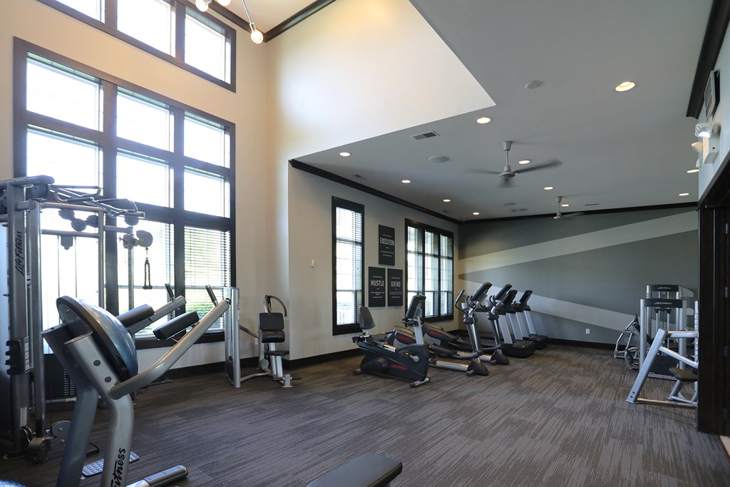 a gym with cardio equipment and large windows