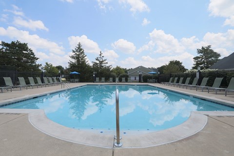 A large outdoor swimming pool with a blue sky and clouds reflected in the water.