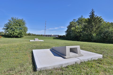 A concrete structure with a rectangular opening sits in a grassy field.