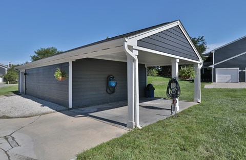 A grey garage with a white roof and a bicycle leaning against it.
