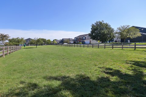 A grassy field with a fence and buildings in the distance.