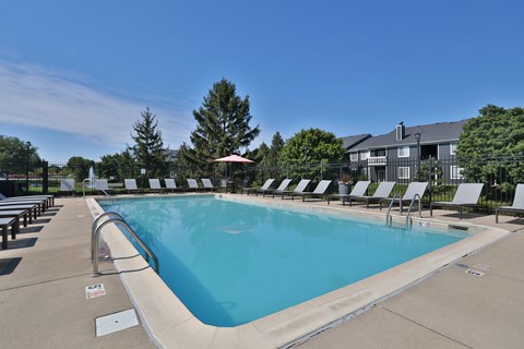 A large outdoor swimming pool with sun loungers and a building in the background.
