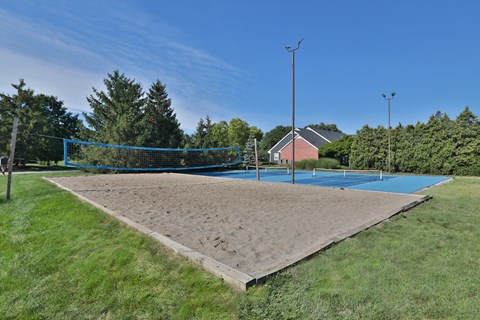 A sand volleyball court with a blue net and a blue sky in the background.