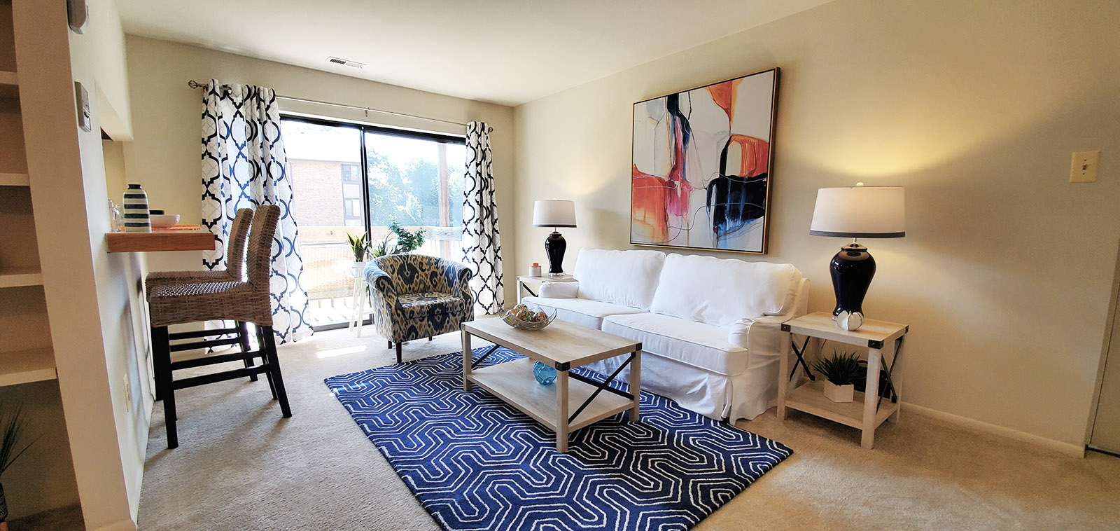 A living room with a white couch, a blue rug, and a painting on the wall.