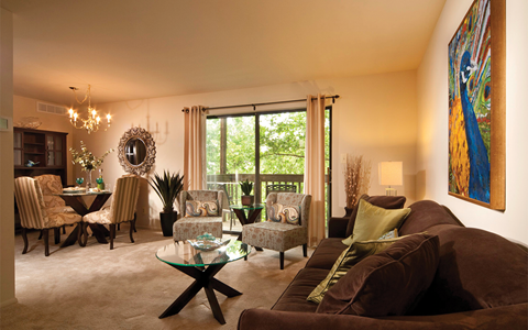 A living room with a glass coffee table and a large painting on the wall.