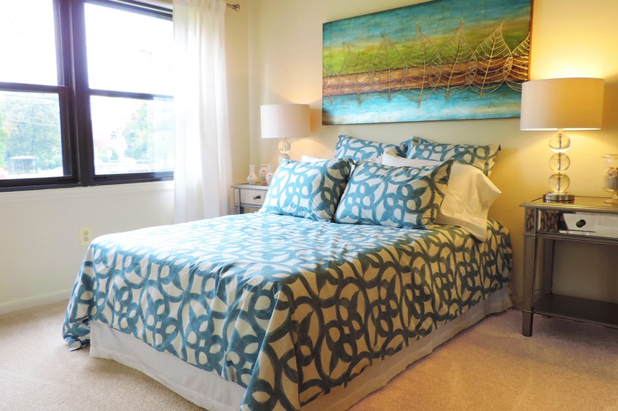 A bed with a blue and black comforter and pillows sits in a room with a painting on the wall.