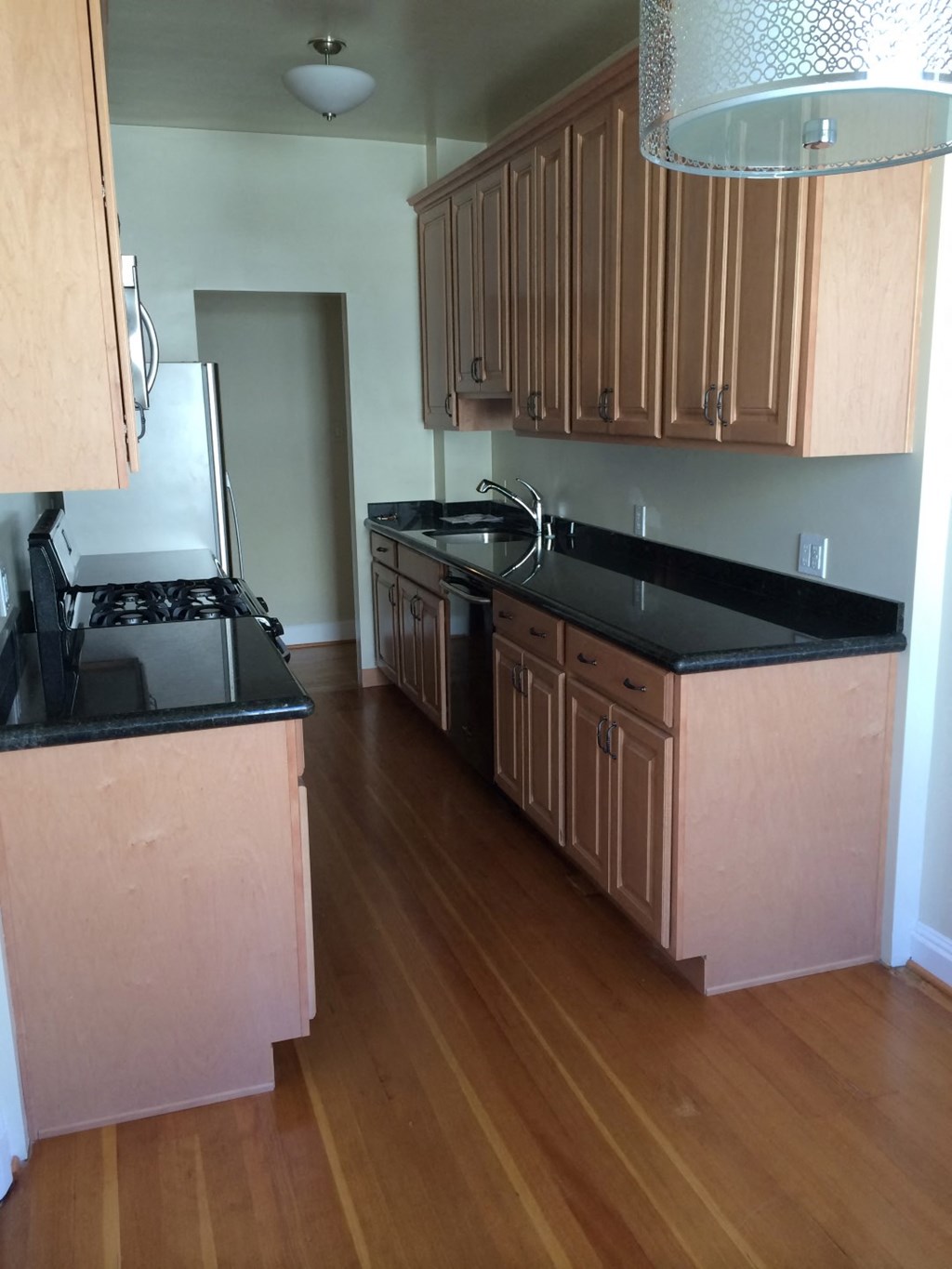 an empty kitchen with black counter tops and wooden floors