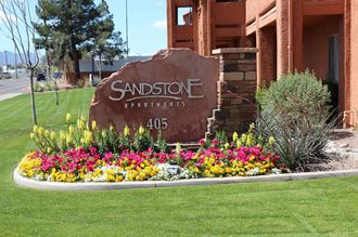 the sign for the sandstone apartments in front of a flower garden