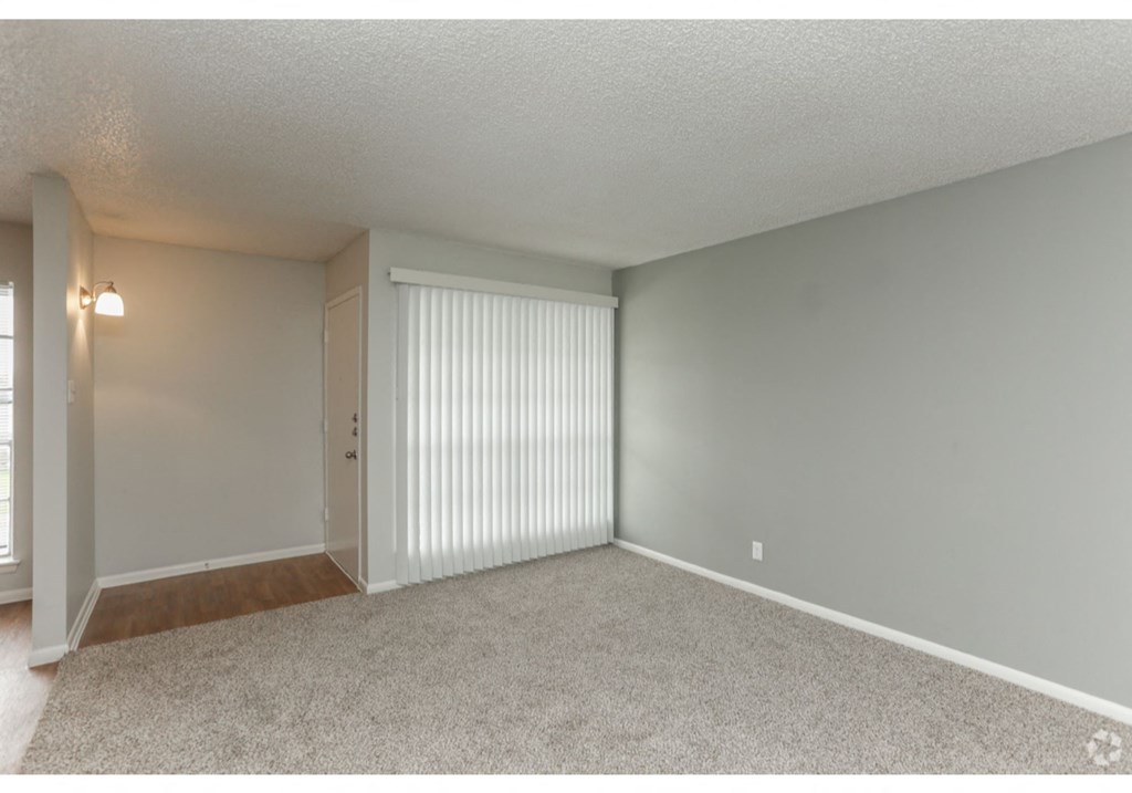 an empty living room with white blinds and a door to a closet