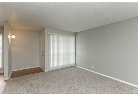 an empty living room with white blinds and a door to a closet