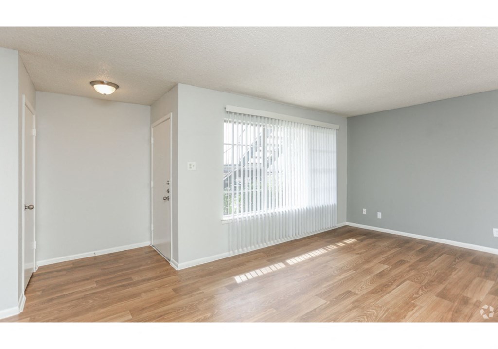 an empty living room with a large window and wood flooring