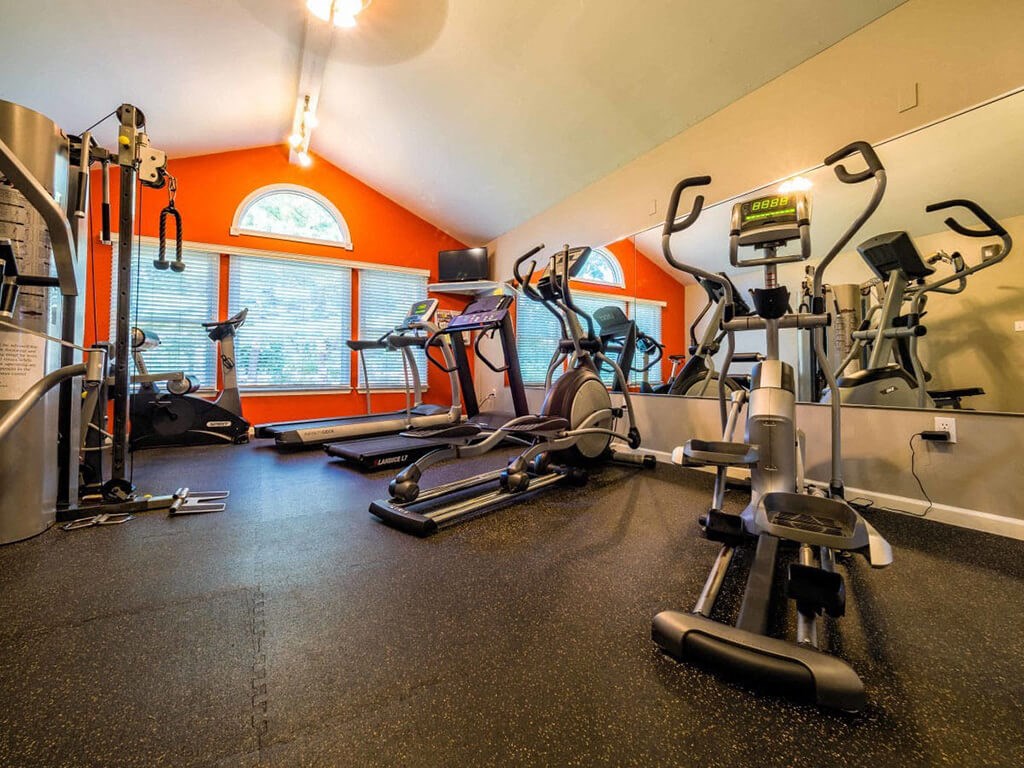 a gym with weights and cardio equipment on the floor and a window