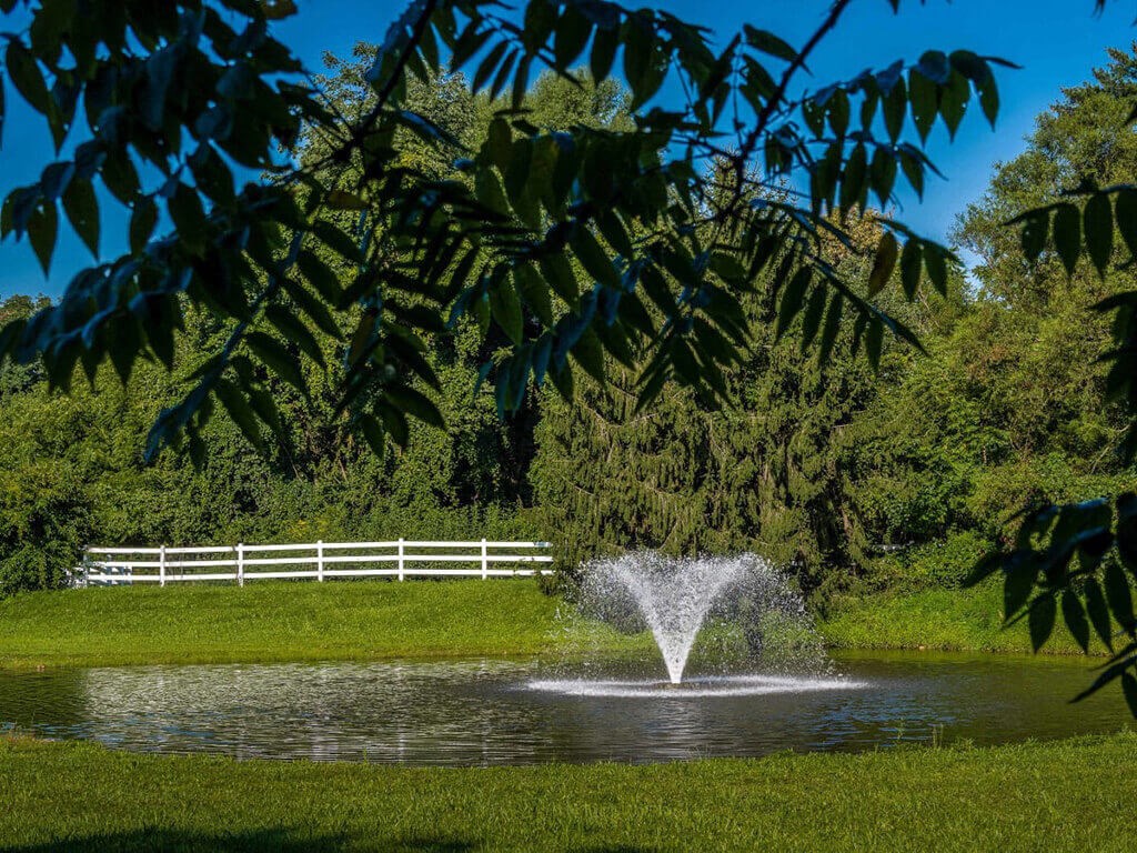 a fountain in a pond with a white fence