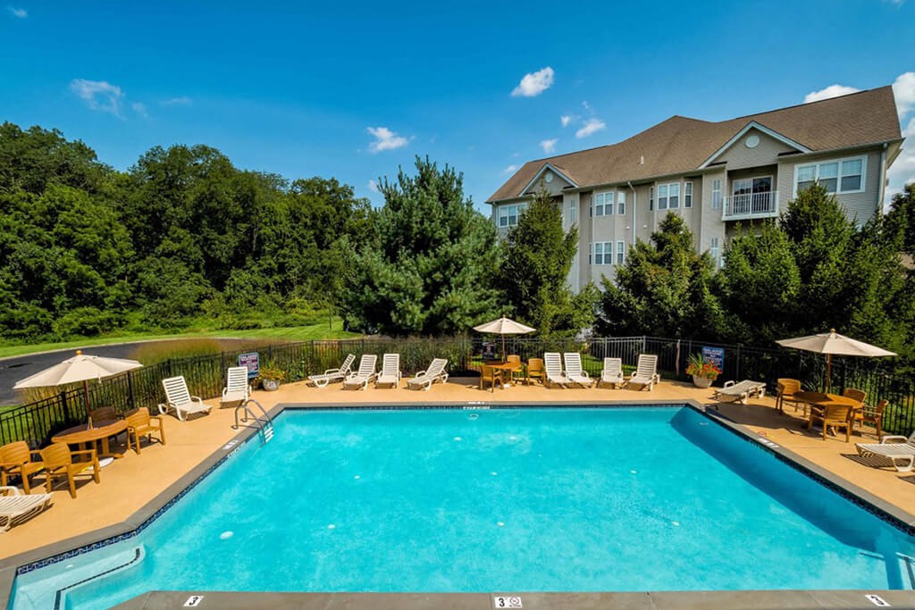 a swimming pool with chairs and umbrellas and a building in the background