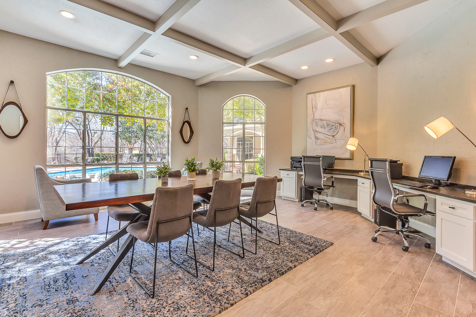 Business center boasting natural lighting and large windows with conference table, computers and printer